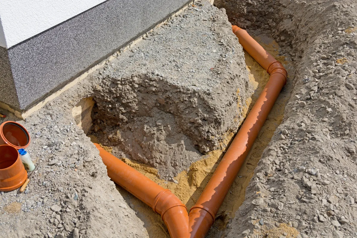 Travaux de raccordement de canalisations effectués par une entreprise de plomberie, avec tuyaux enterrés et tranchées ouvertes.